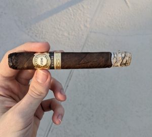 Hand holding a Perla Del Mar Maduro cigar ashed at the end
